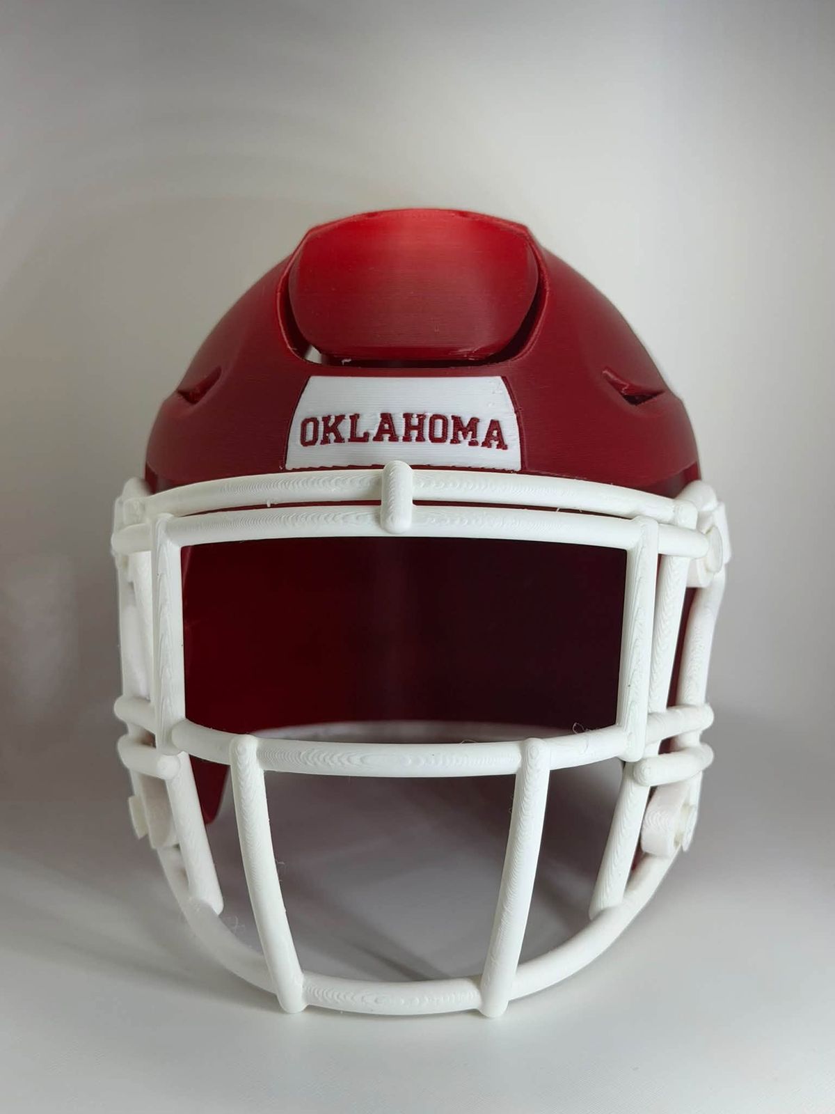 Front view of the same miniature red OU football helmet, with &ldquo;OKLAHOMA&rdquo; across the front and a white face mask