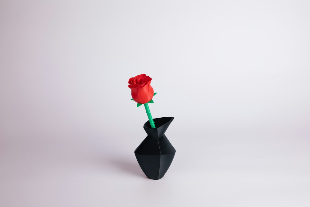 A 3D printed red rose in a black geometric vase